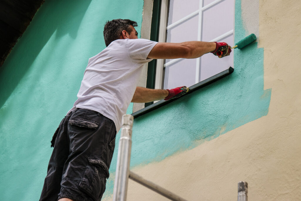 A worker paints the facade walls of a house with paint using a paint roller